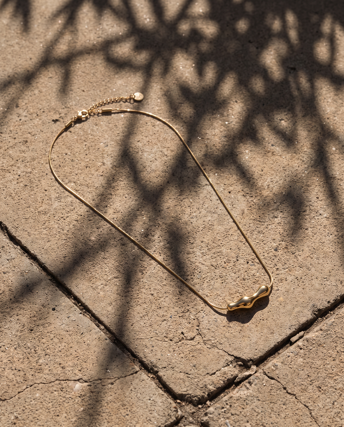 Aura Necklace goudkleurige waterproof RVS ketting op een betonnen ondergrond in natuurlijk zonlicht.