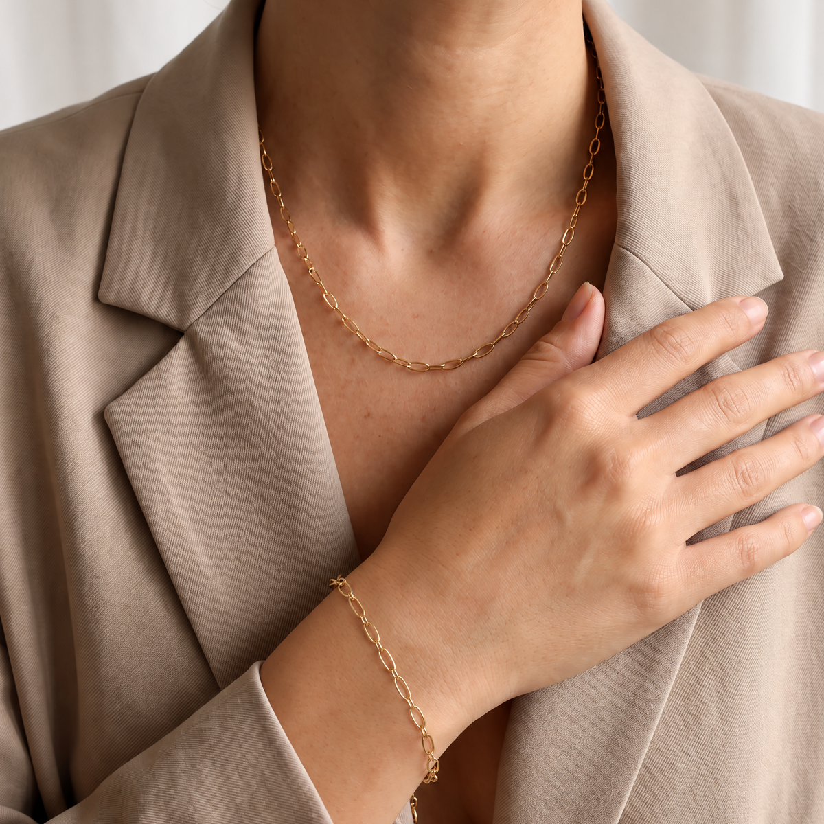 Goudkleurige Luna Set van Gioia store met een minimalistische RVS schakelketting en goudkleurige RVS schakelarmband, gedragen bij een beige blazer.
