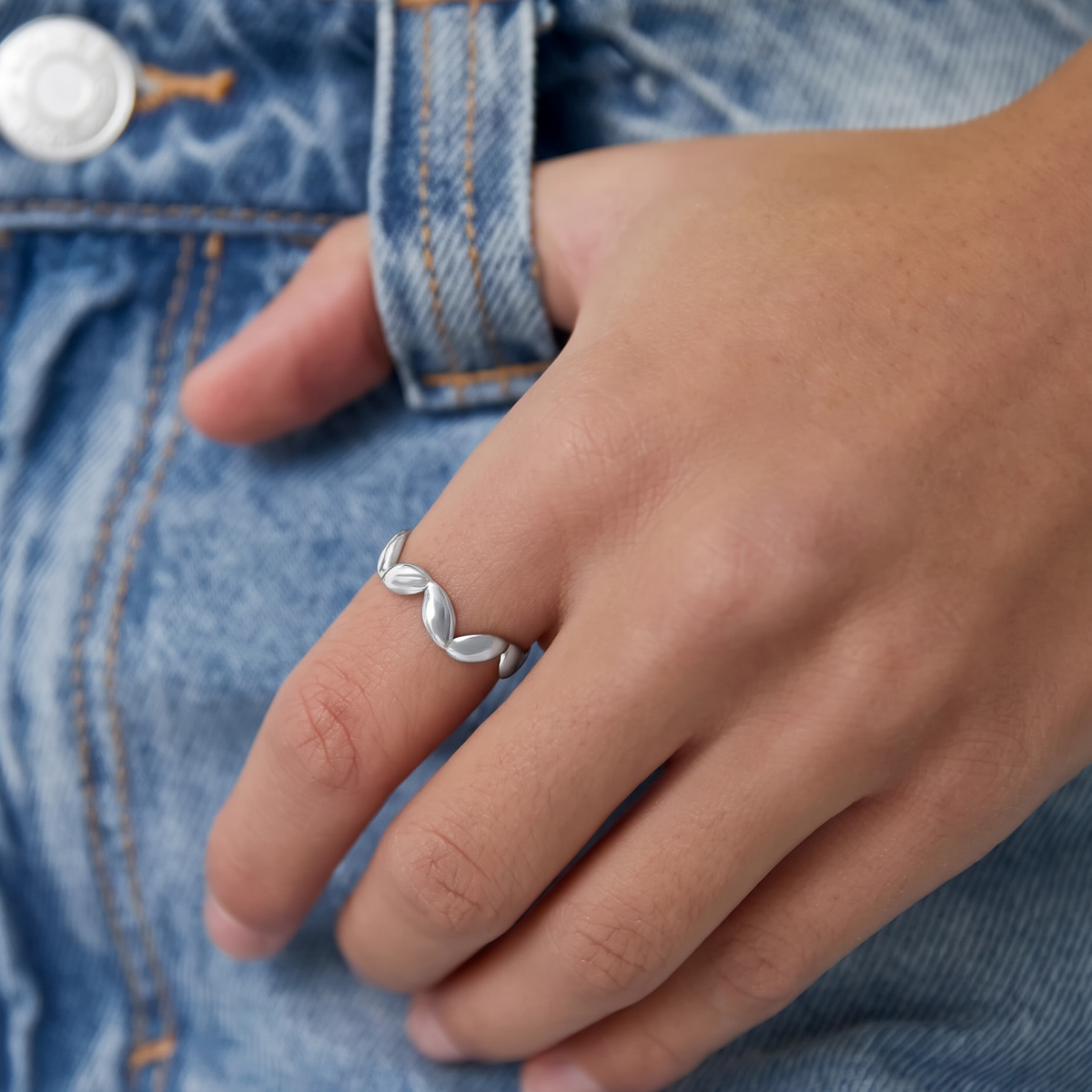 Minimalistische zilveren Petal Ring van RVS gedragen aan een hand met blauwe denim jeans.