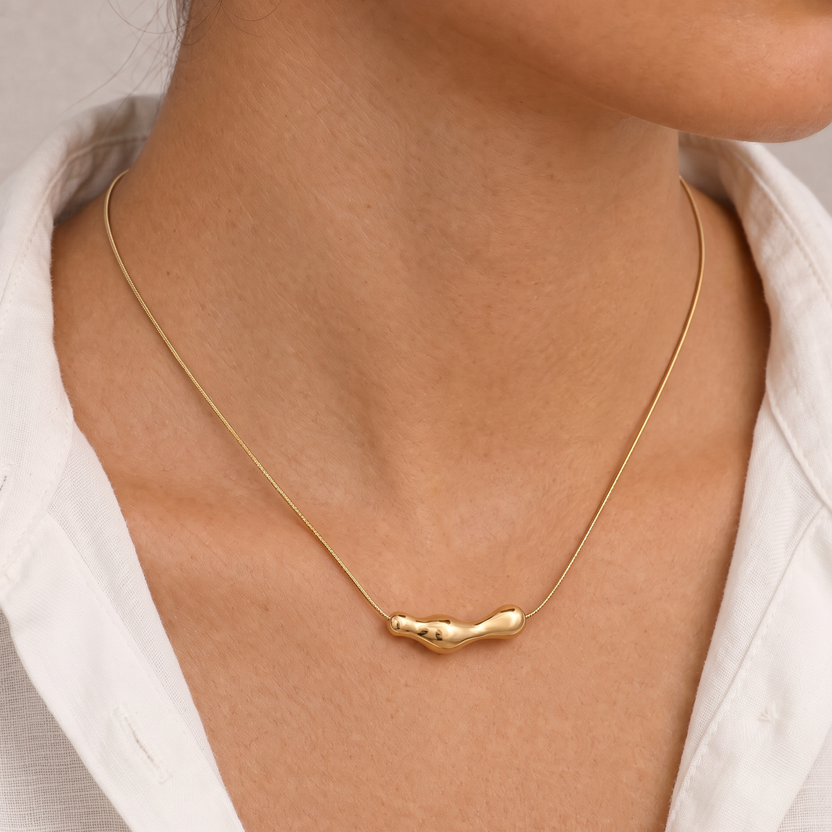 Vrouw draagt de Aura Necklace goudkleurige RVS ketting met organische hanger en minimalistische snake chain.