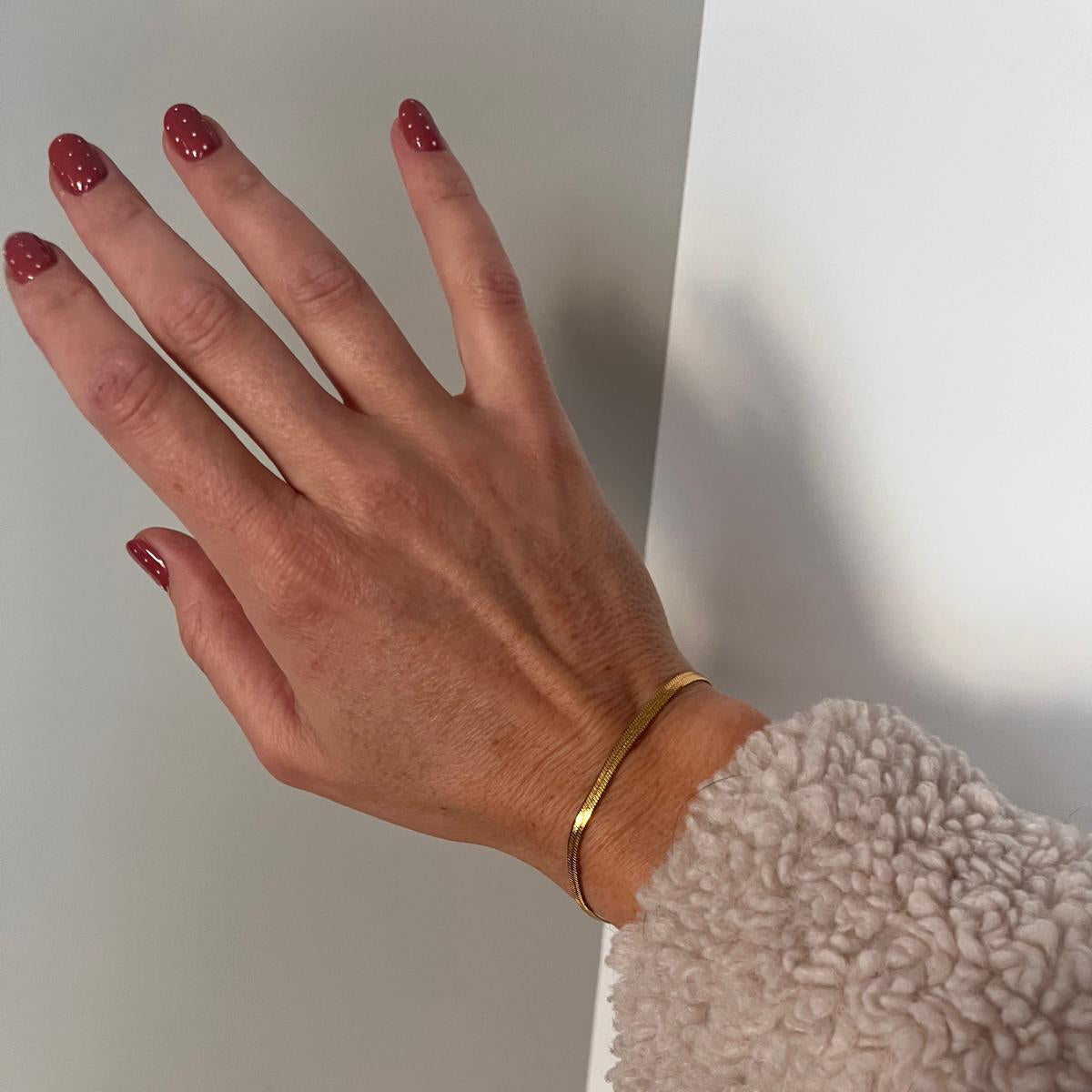 Vrouwen arm en hand met snake chain armband in goud.