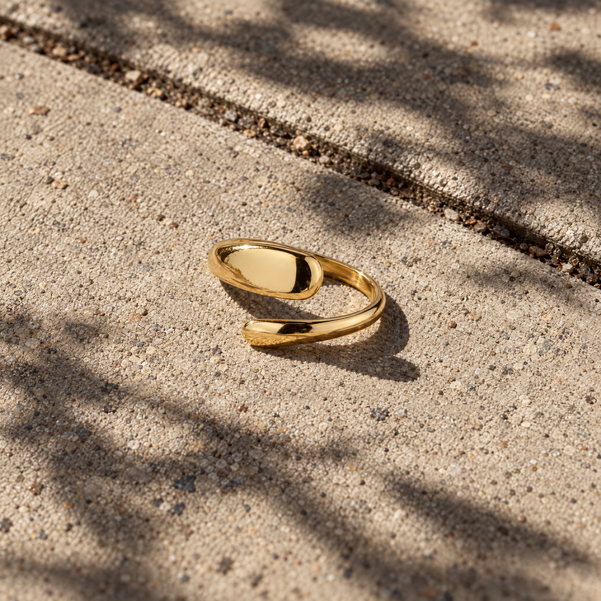 Flow Ring in goudkleurig roestvrij staal (RVS) met organische golvende vorm, gefotografeerd op een betonnen ondergrond. Minimalistische damesring voor dagelijks gebruik.