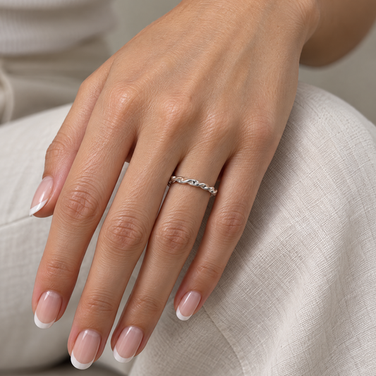 Zilveren gedraaide roestvrijstalen ring op een hand met minimalistische beige outfit.