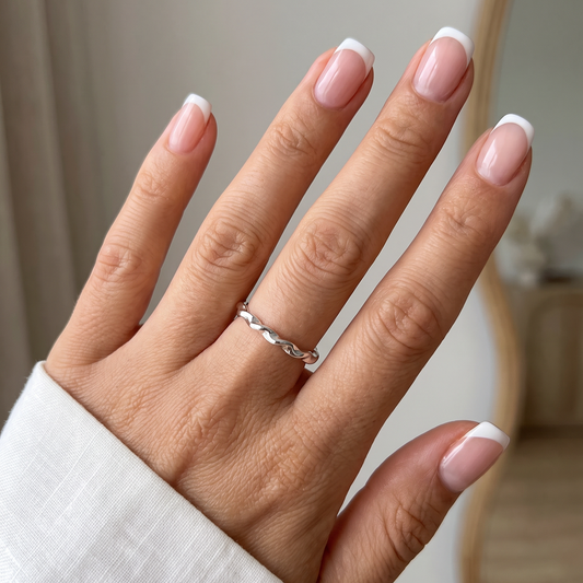 Minimalistische zilveren gedraaide RVS ring gedragen aan een hand met French manicure.