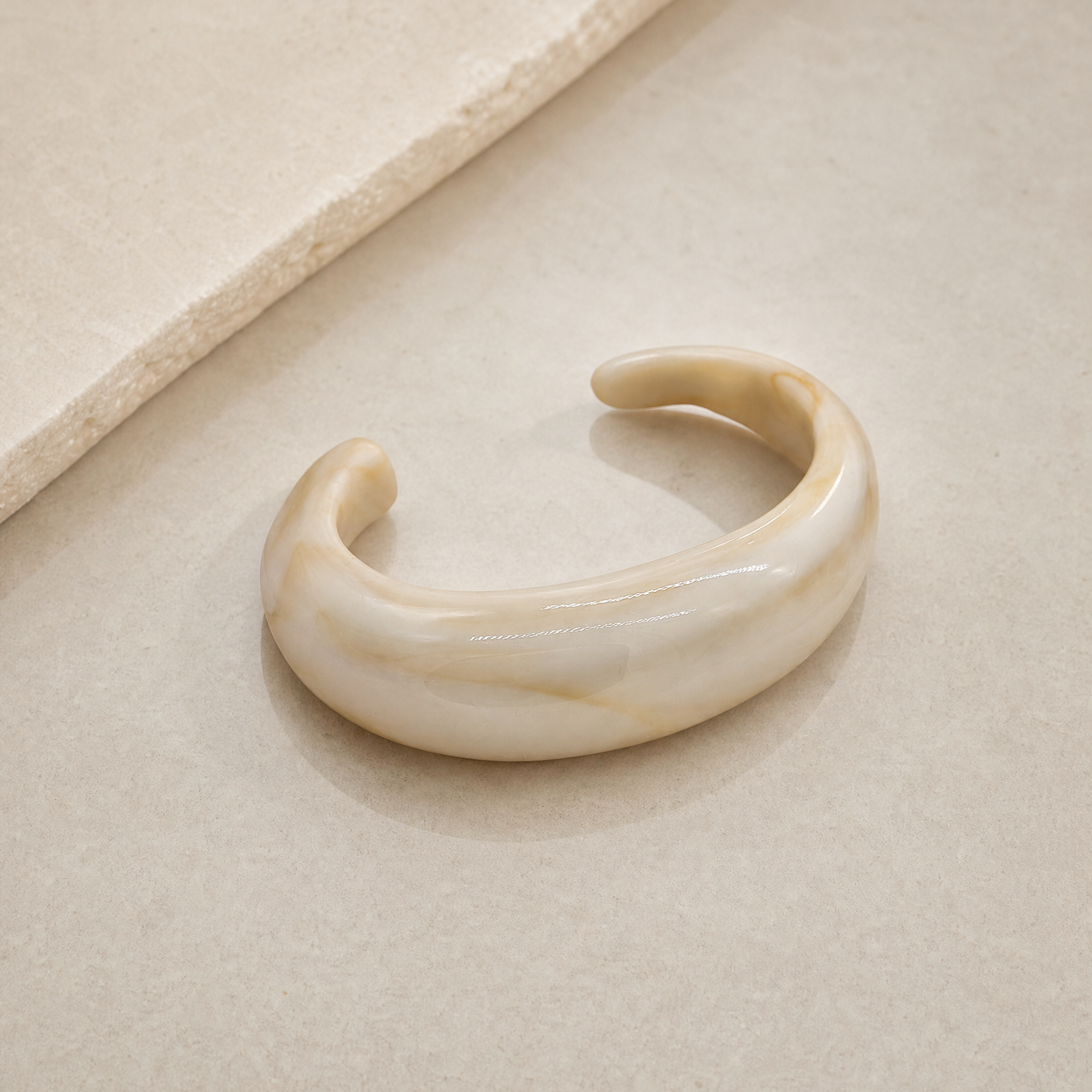 The soft stond bangle in offwhite met een beige marmering erin. Het design is een open bangle dit dikker is in het midden en taps toeloopt richting de einden. Gemaakt van hars, dus lichtgewicht en comfortabel