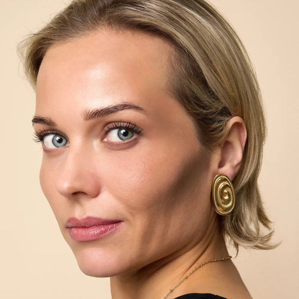 Blonde vrouw die organische statement oorbellen in ovale vorm draagt. Gemaakt van hoogwaardig stainless steel in de kleur goud.