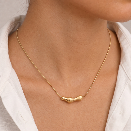 Vrouw draagt de Aura Necklace goudkleurige RVS ketting met organische hanger en minimalistische snake chain.