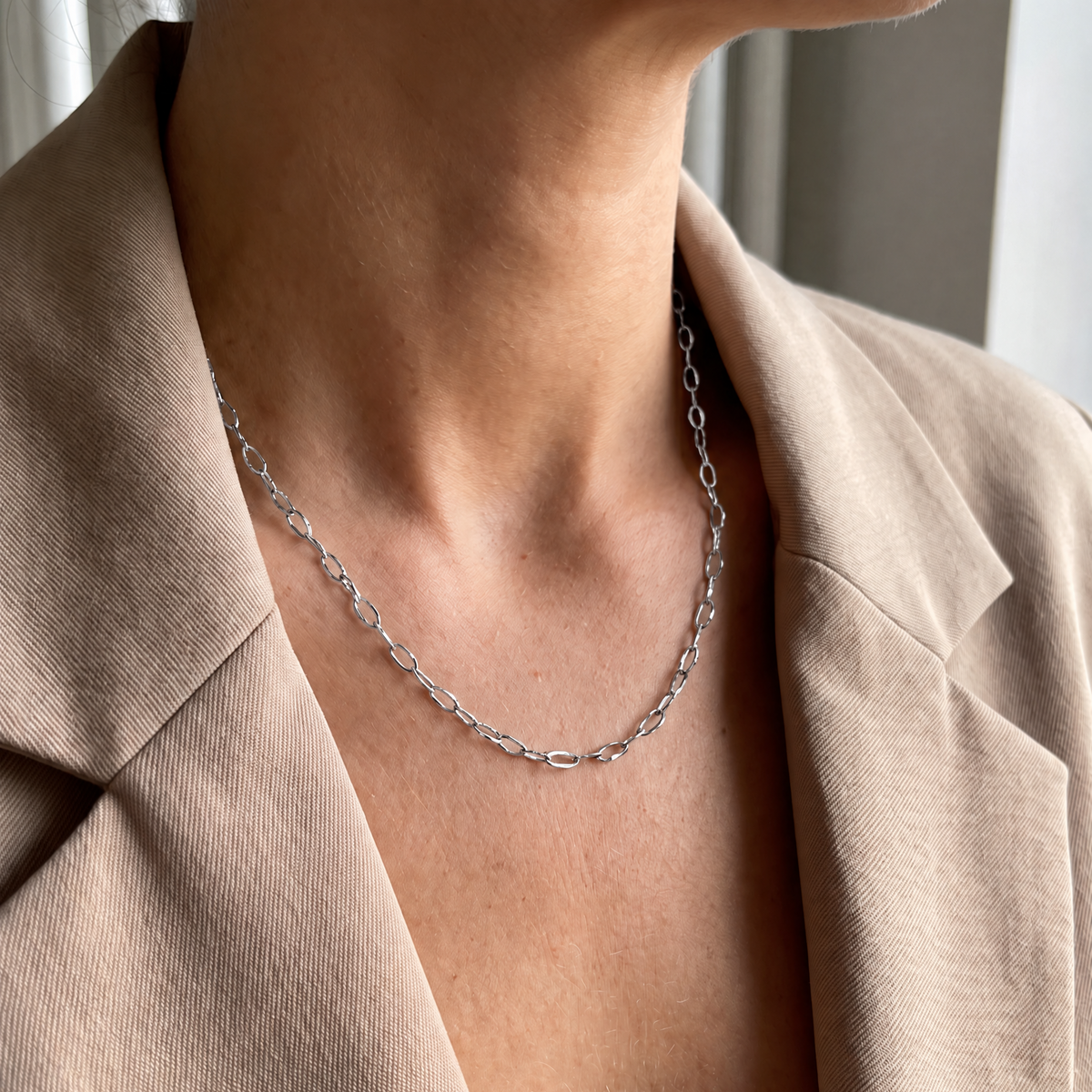 Close-up van een vrouw die de Luna Chain zilverkleurige waterproof RVS schakelketting draagt met een beige blazer.