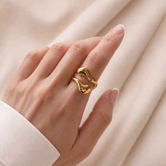 Minimalistische goudkleurige verstelbare RVS ring met vloeiende organische vorm gedragen aan een hand.