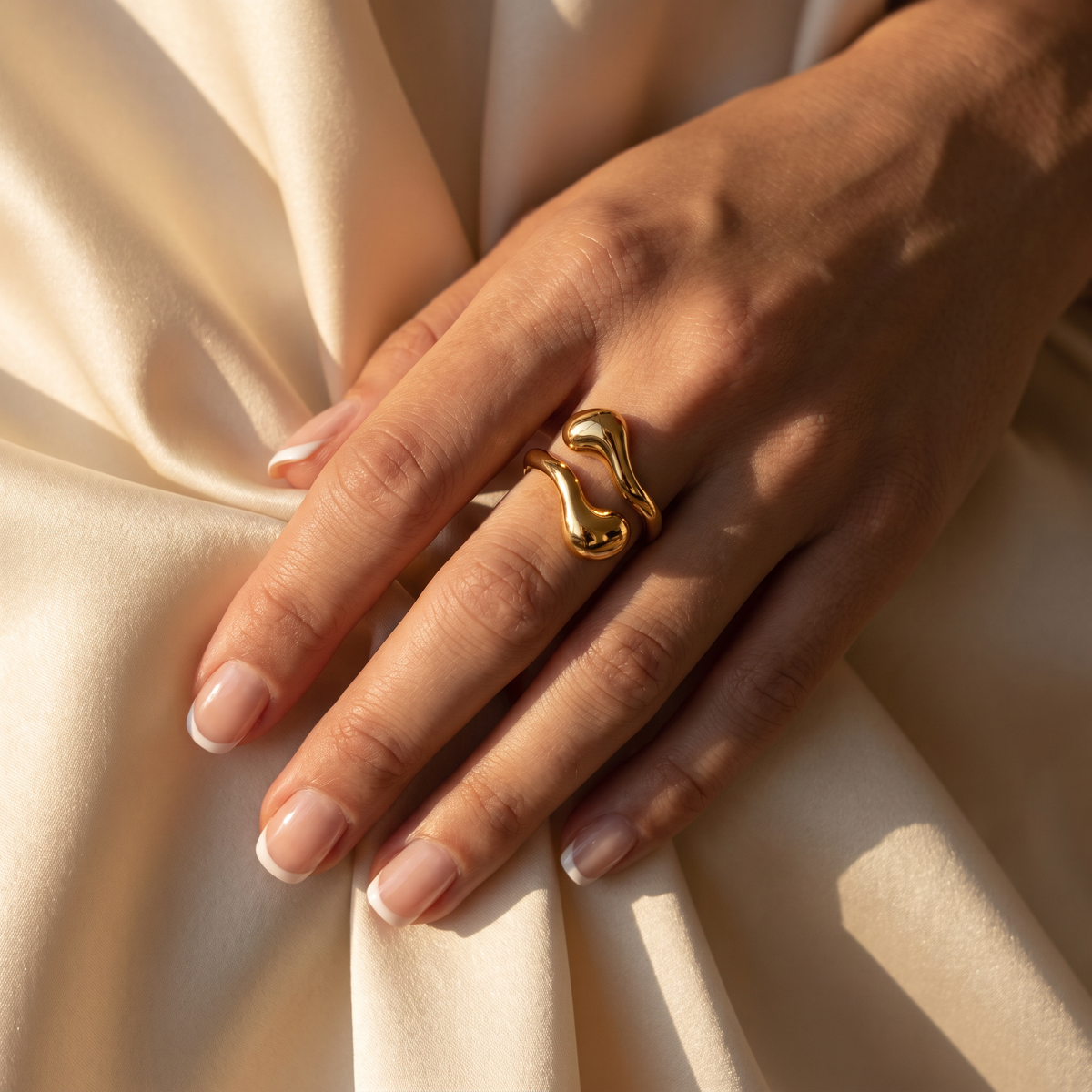 Goudkleurige Aura Ring van RVS met organische sculpturale vorm gedragen aan een hand op satijnen stof.