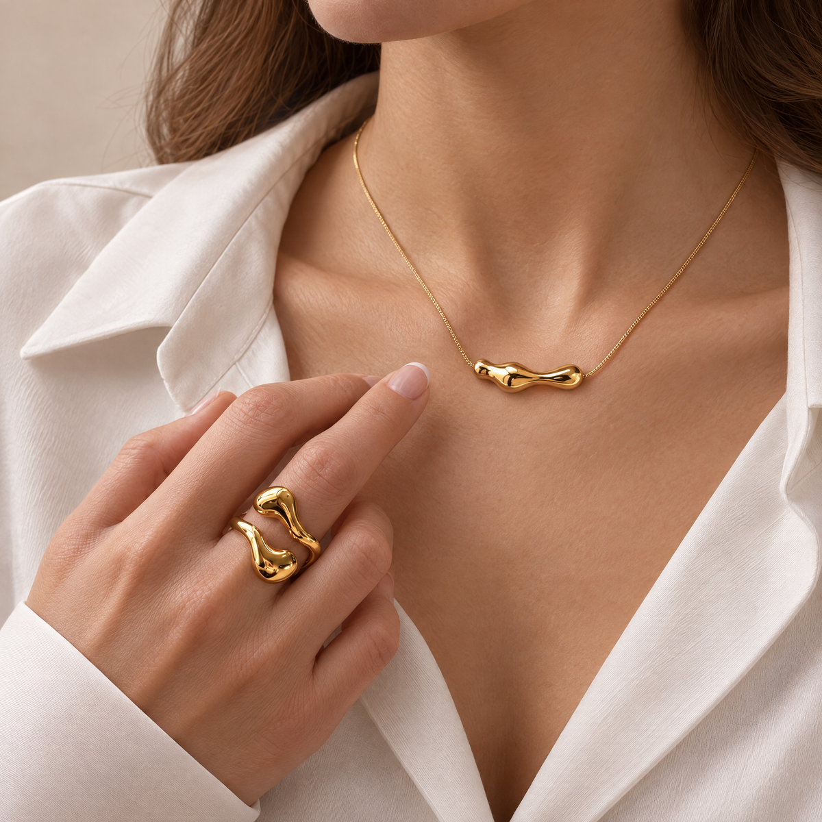 Goudkleurige Aura Set van Gioia store met een minimalistische RVS ketting en verstelbare RVS ring gedragen bij een witte blouse.