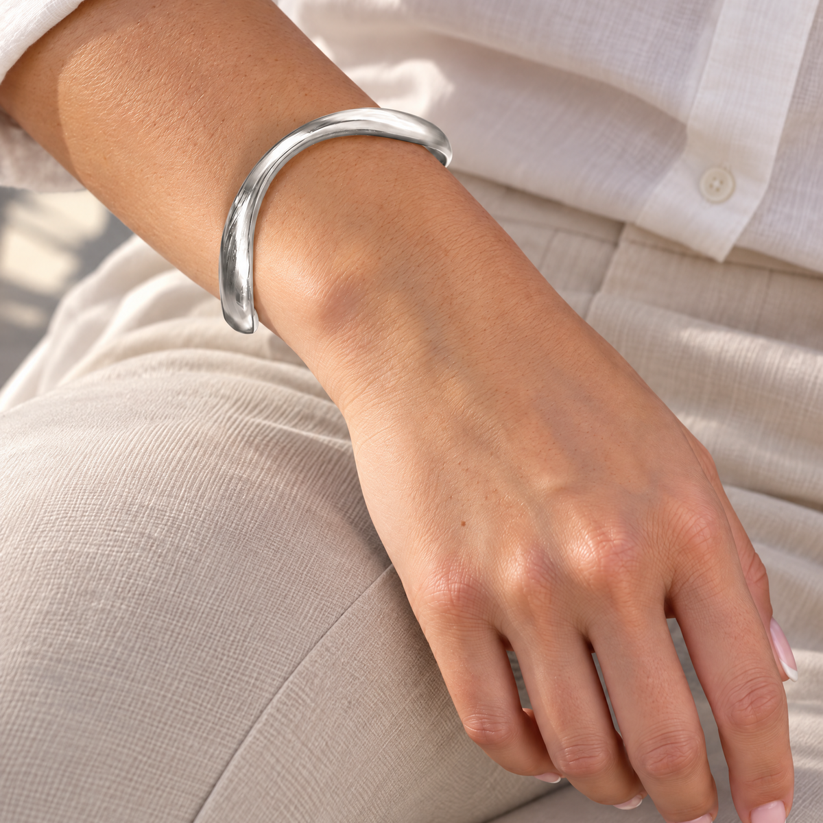 Vrouw draagt de Organic Bangle zilverkleurige RVS armband met organisch design en een witte linnen outfit.